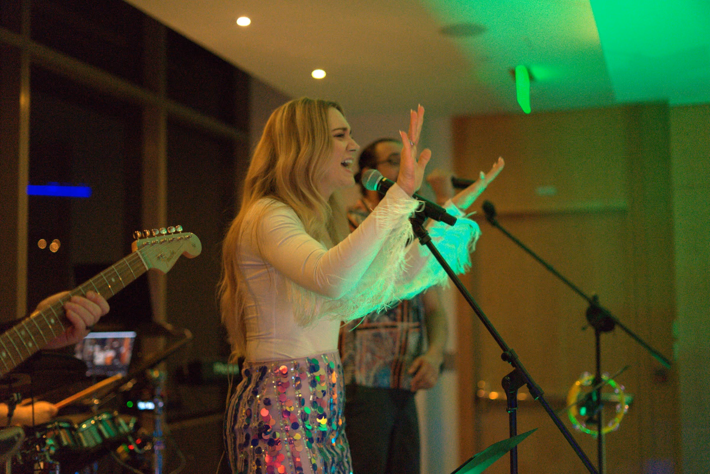 Two vocalists at their microphones with the band spread across a window-lined room